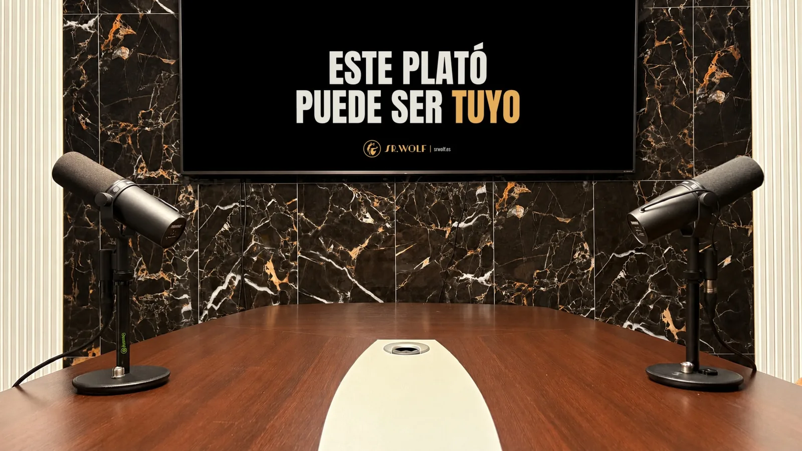 Plató de Sr. Wolf: pared de mármol negro con vetas doradas, dos micrófonos de estudio y una mesa de madera. En la pantalla de la pared: «Este plató puede ser tuyo».